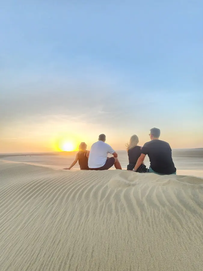 Three guests watching the sun go down from the crest of a dune